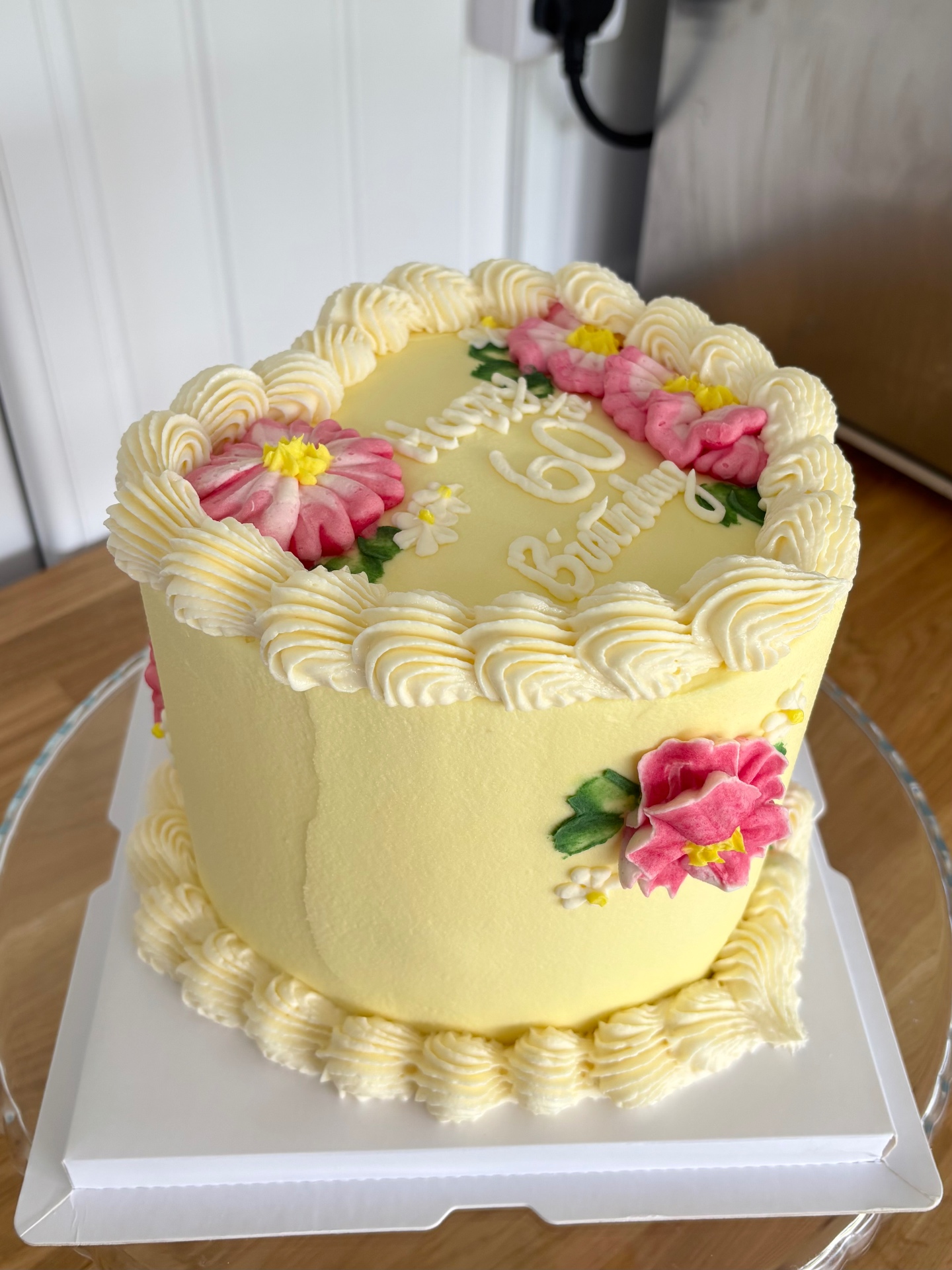 Heart-shaped yellow buttercream birthday cake with piped pink flowers, daisies and cream rosettes