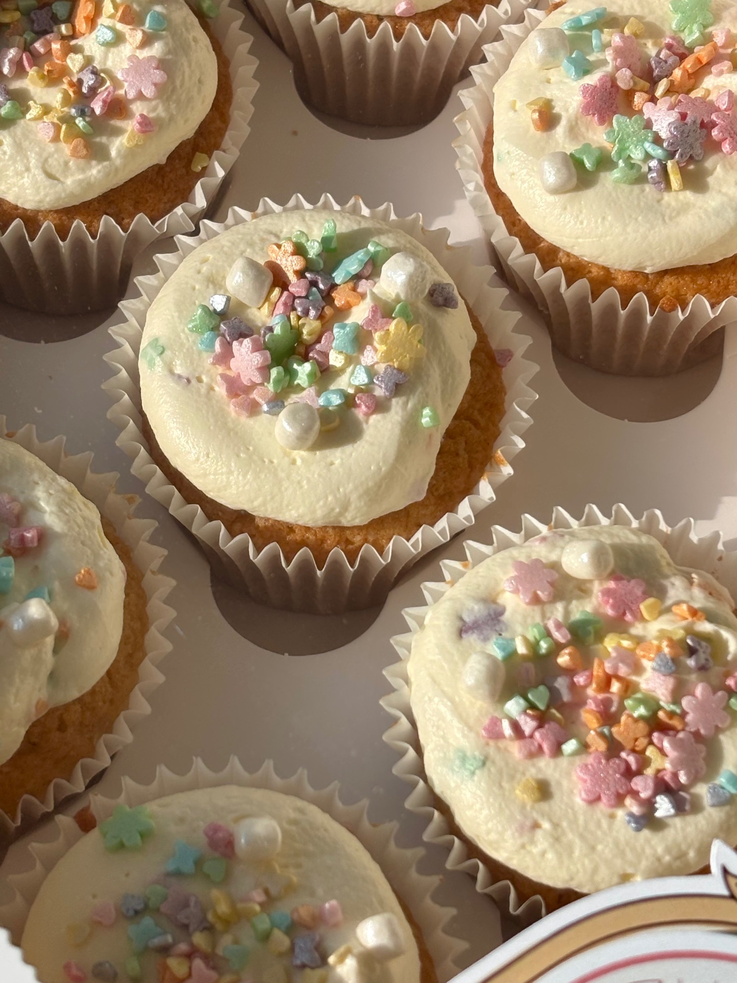 Box of vanilla cupcakes topped with pastel sprinkles, sugar pearls and star-shaped confetti