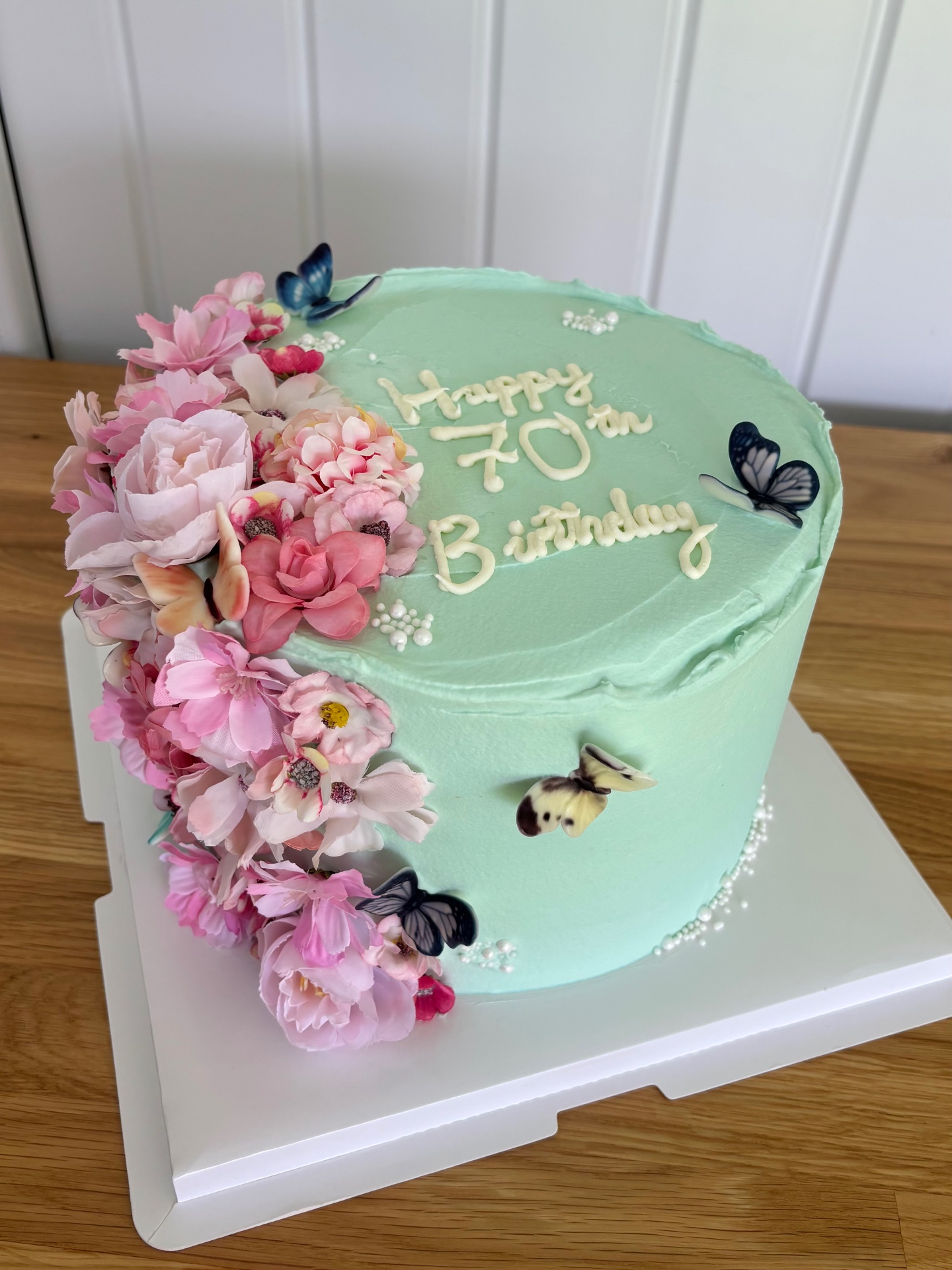 Mint green 70th birthday cake decorated with pink sugar flowers and butterflies