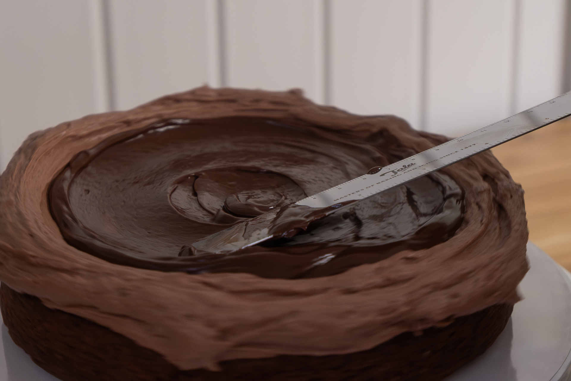 Chocolate ganache being smoothed over a freshly iced chocolate cake