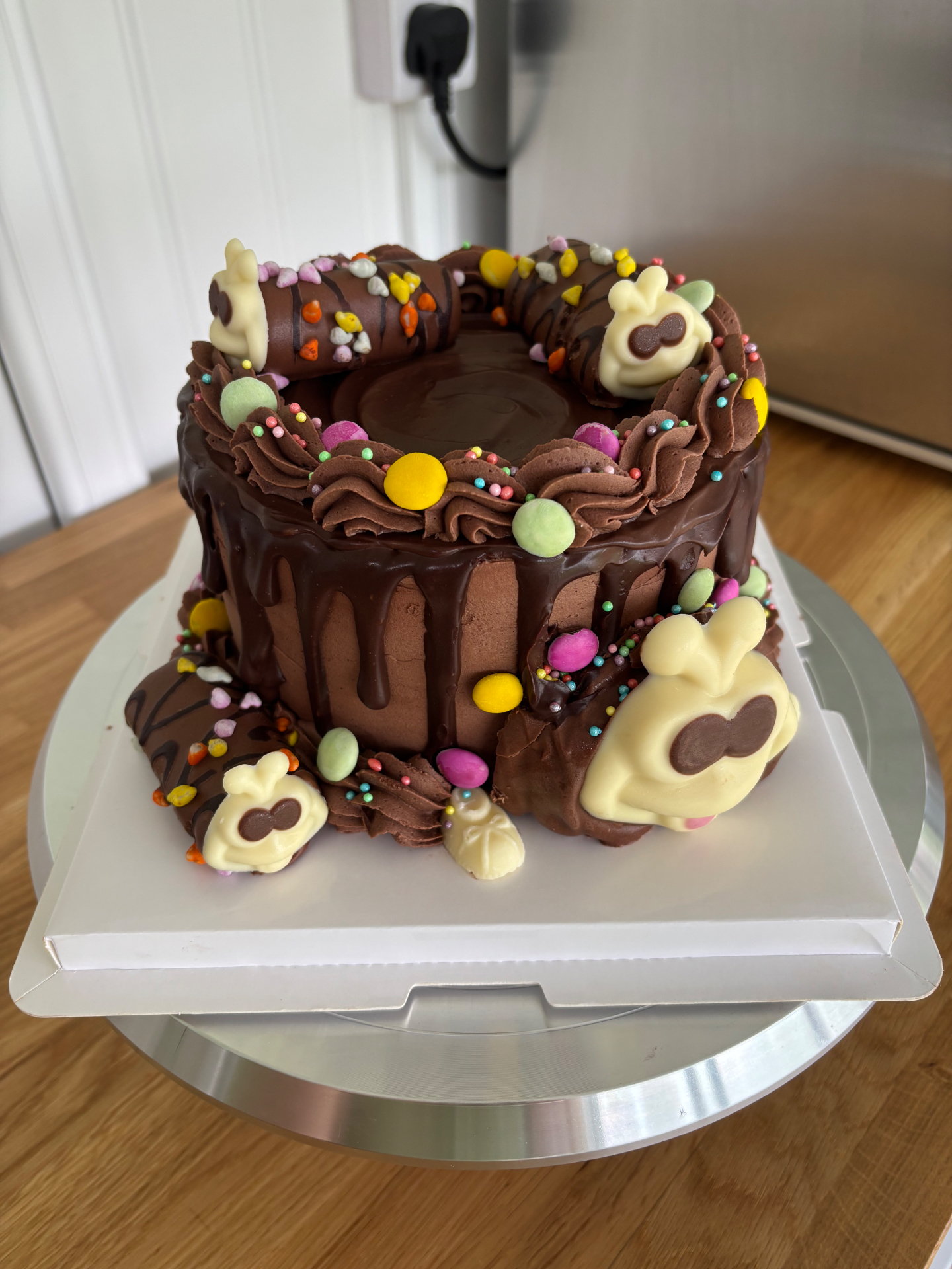 Chocolate drip cake topped with colourful candy eggs, sprinkles and white chocolate bunnies