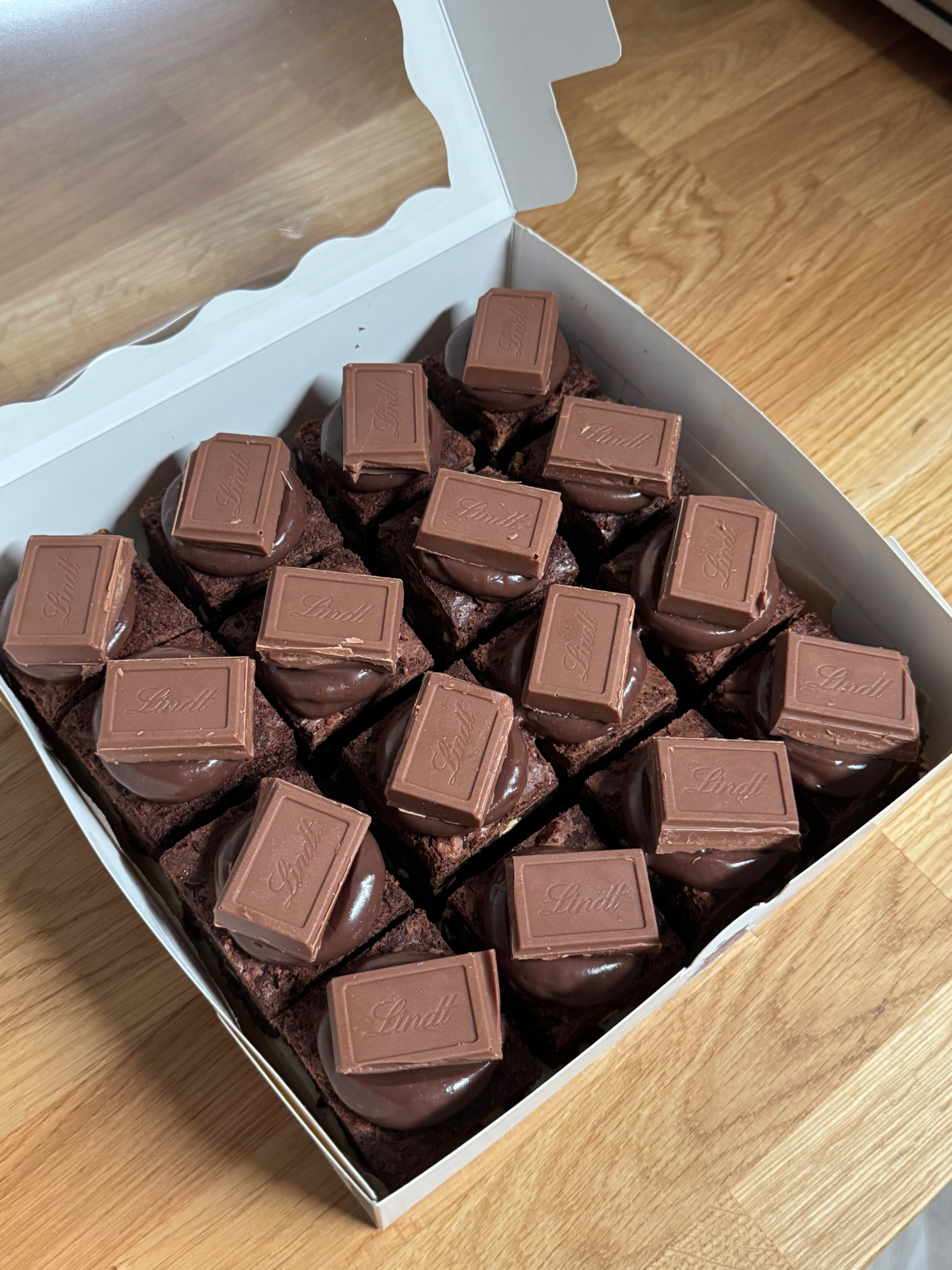 Box of fudgy brownies piped with chocolate ganache and topped with Lindt chocolate squares