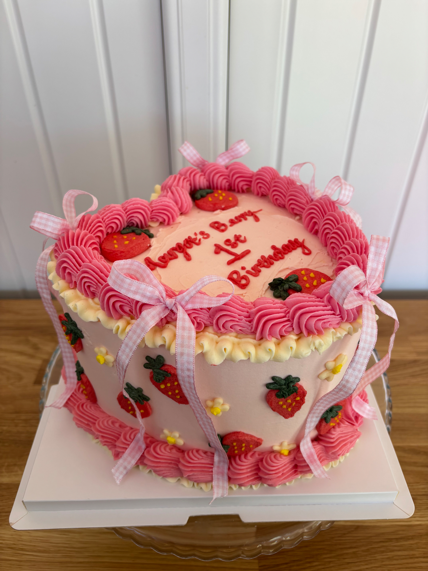 Pink strawberry birthday cake with piped ruffles, gingham bows and sugar strawberries