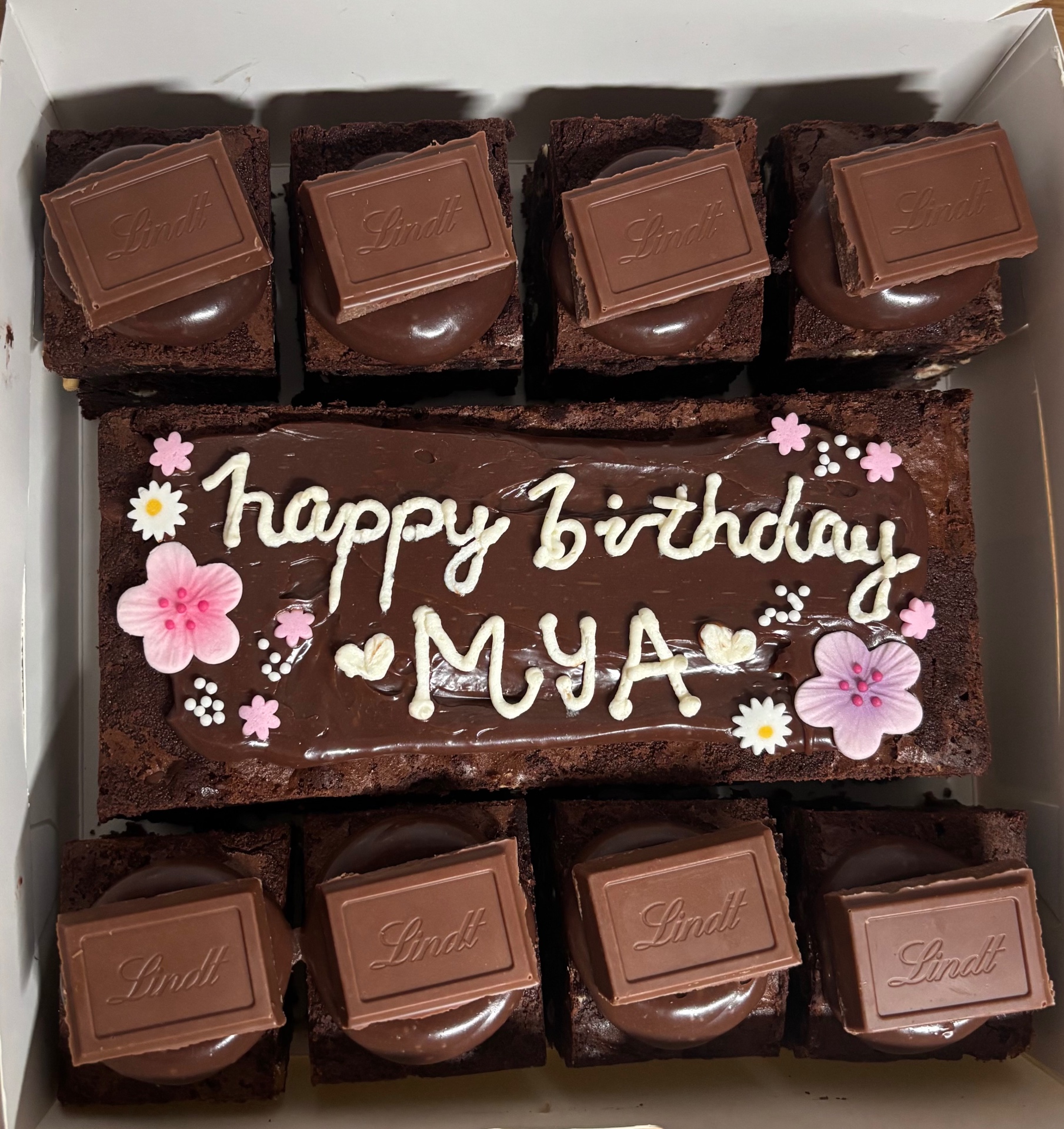 Brownie gift box with 'happy birthday MYA' piped on a ganache slab, cherry blossom sugar flowers and Lindt-topped brownie bites
